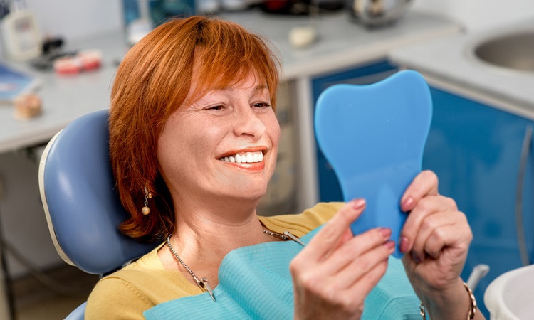 Frau beim Zahnarzt bewundert ihre glänzenden Zähne. 
